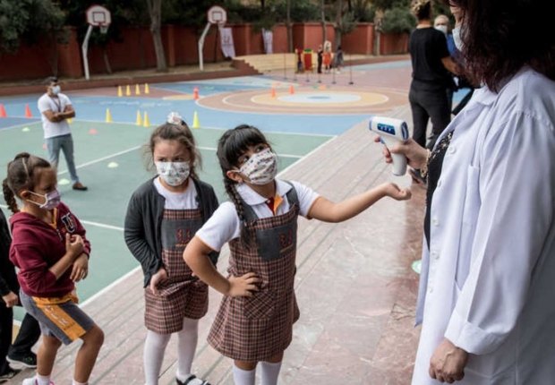 طلبة يرتدون أقنعة واقية لقياس درجة حرارتهم قبل دخول مدرسة بإسطنبول