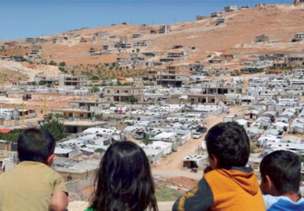 أطفال لبنانيون ينظرون على مخيم سوري في بلدة عرسال الحدودية اللبنانية الشرقية (أ.ب)