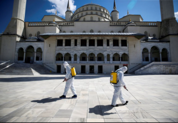 عمال البلدية يرتدون بدلات واقية يقومون بتطهير فناء مسجد في انقرة
