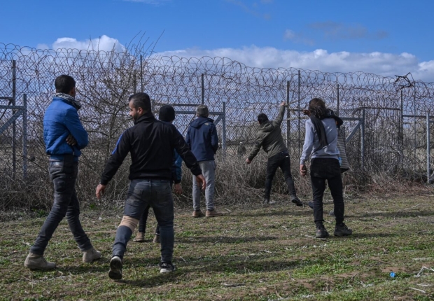 مهاجرون يقفون بالقرب من السياج الحدودي في المنطقة العازلة الحدودية بين تركيا واليونان